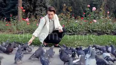 一群鸟在公园里吃面包。 年轻女孩在户外喂鸽子